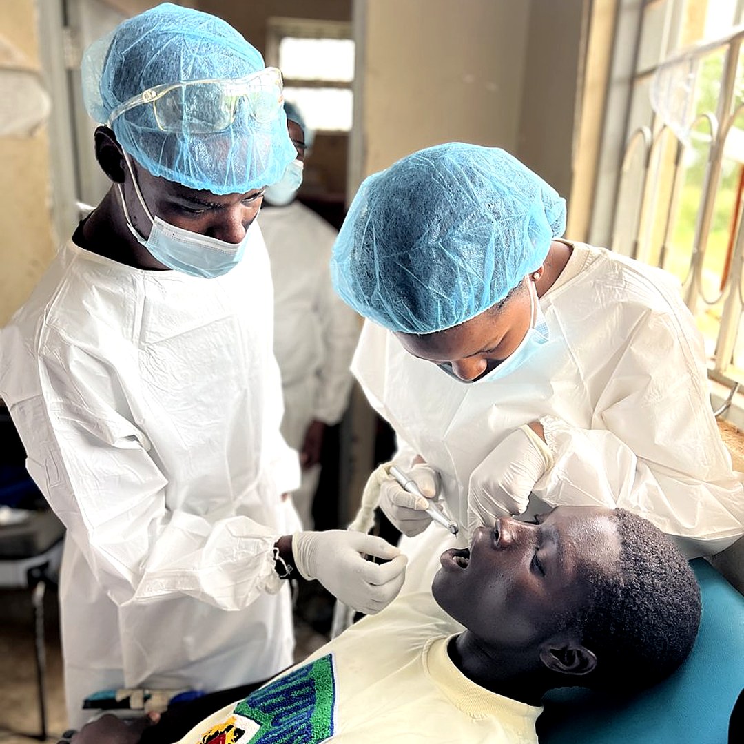 Oral Health Uganda dental outreach team treating a young patient in school uniform during a Northern Uganda community visit — free dental care in Acholi sub-region